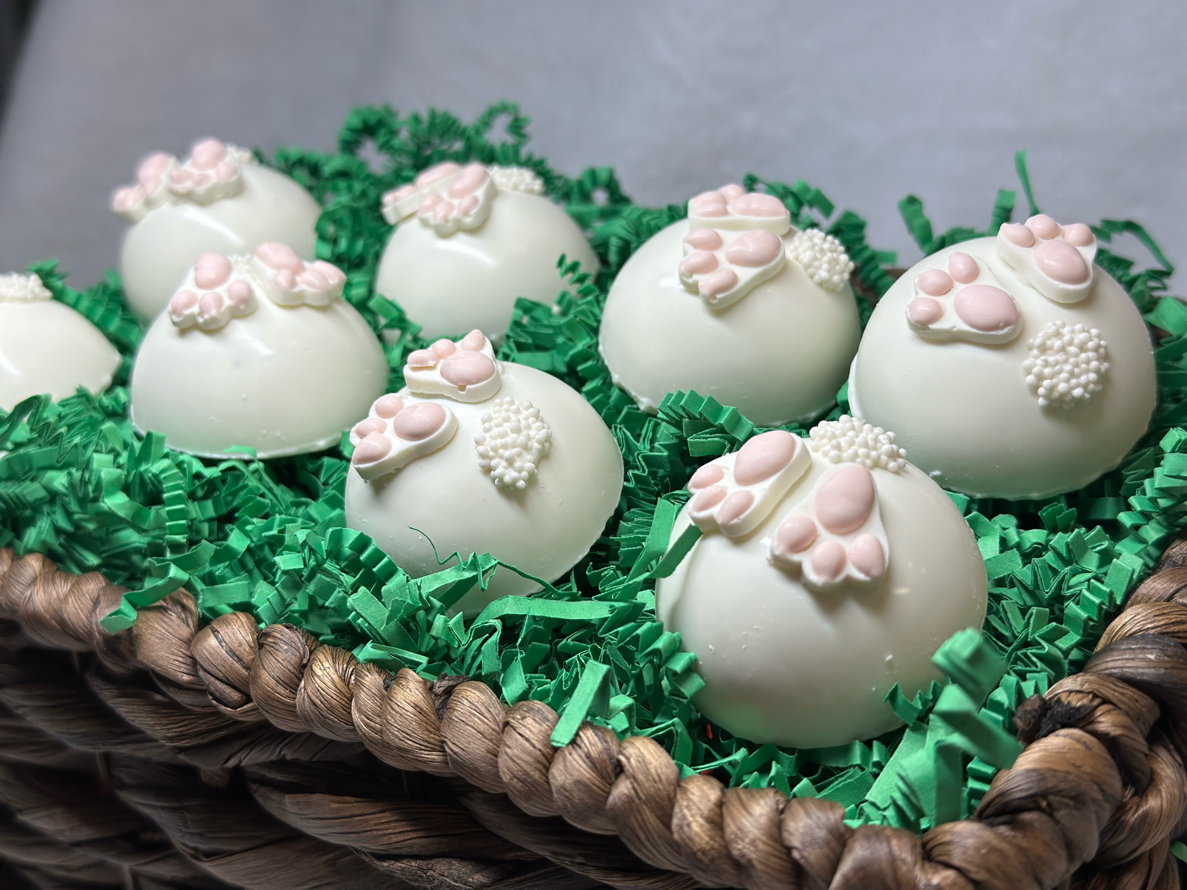 Easter bunny butt cake balls double dipped in white chocolate, arranged in a woven basket on green paper grass