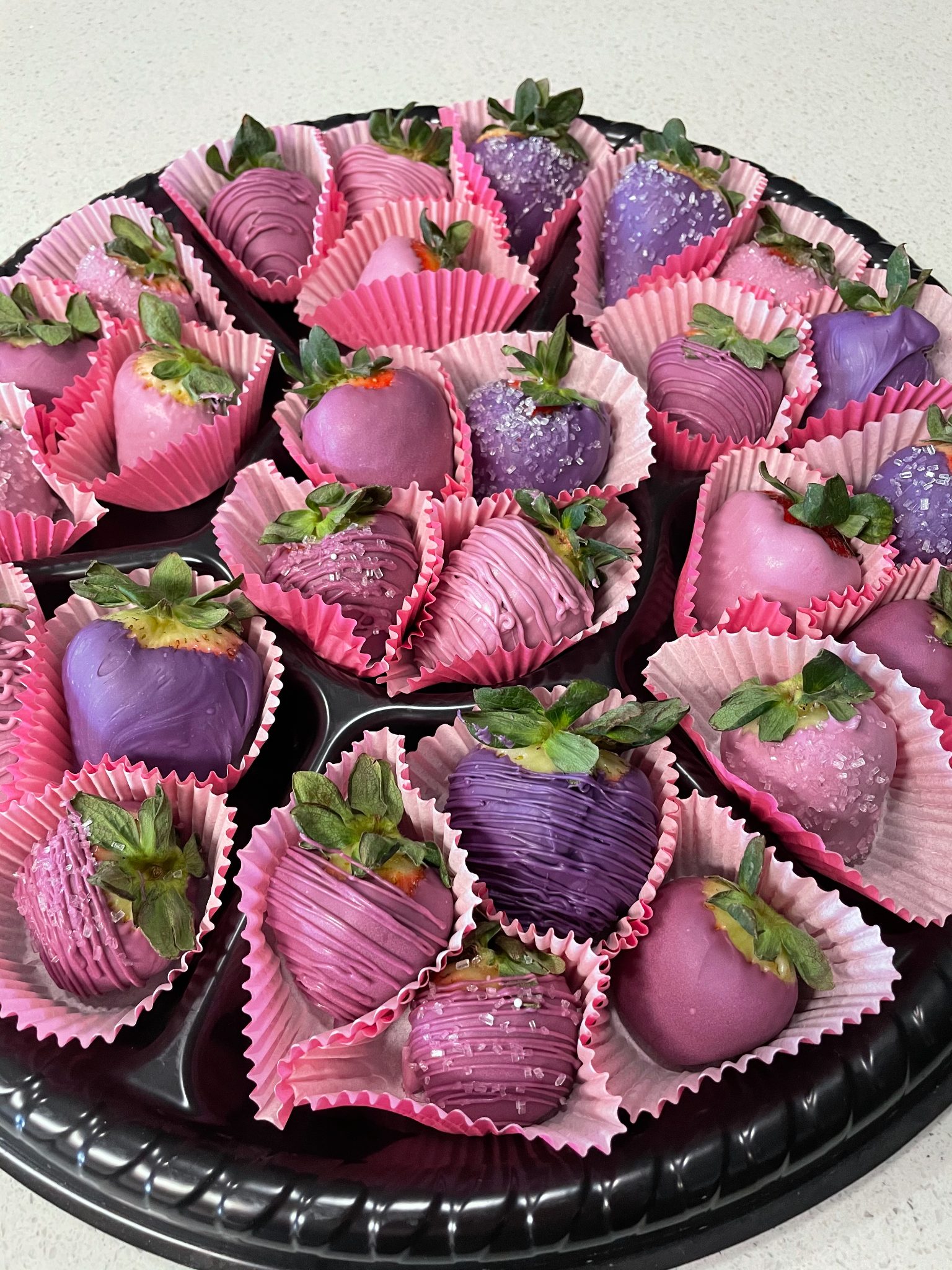 A tray of chocolate covered strawberries in shades of pink and purple with sprinkles