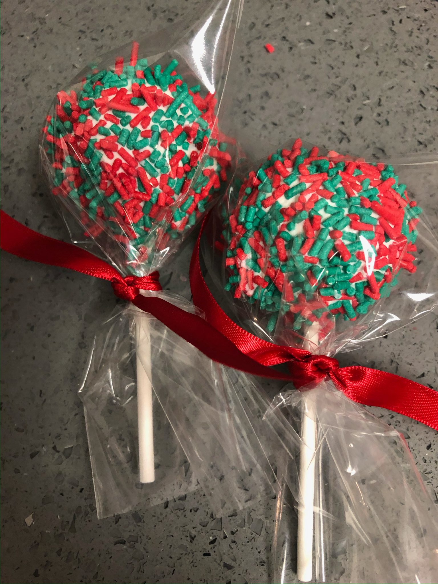 Christmas cake pops wrapped in cellophane with red and green sprinkles and a red ribbon