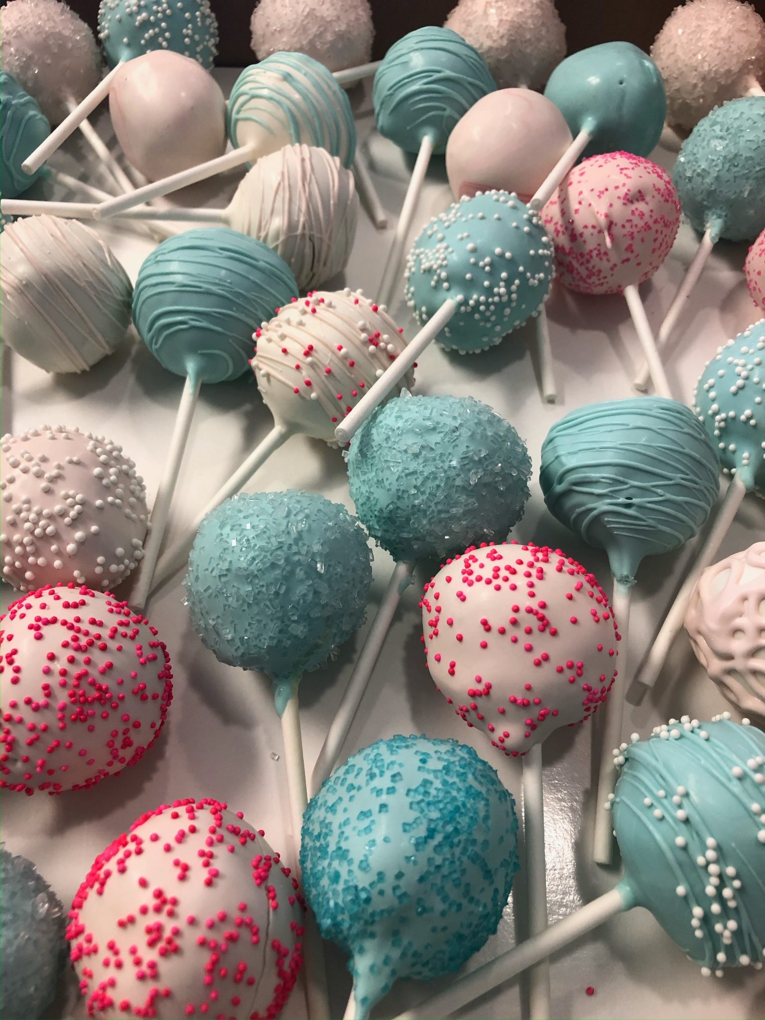 An assortment of teal, white, and pink cake pops with drizzle and sprinkle detail