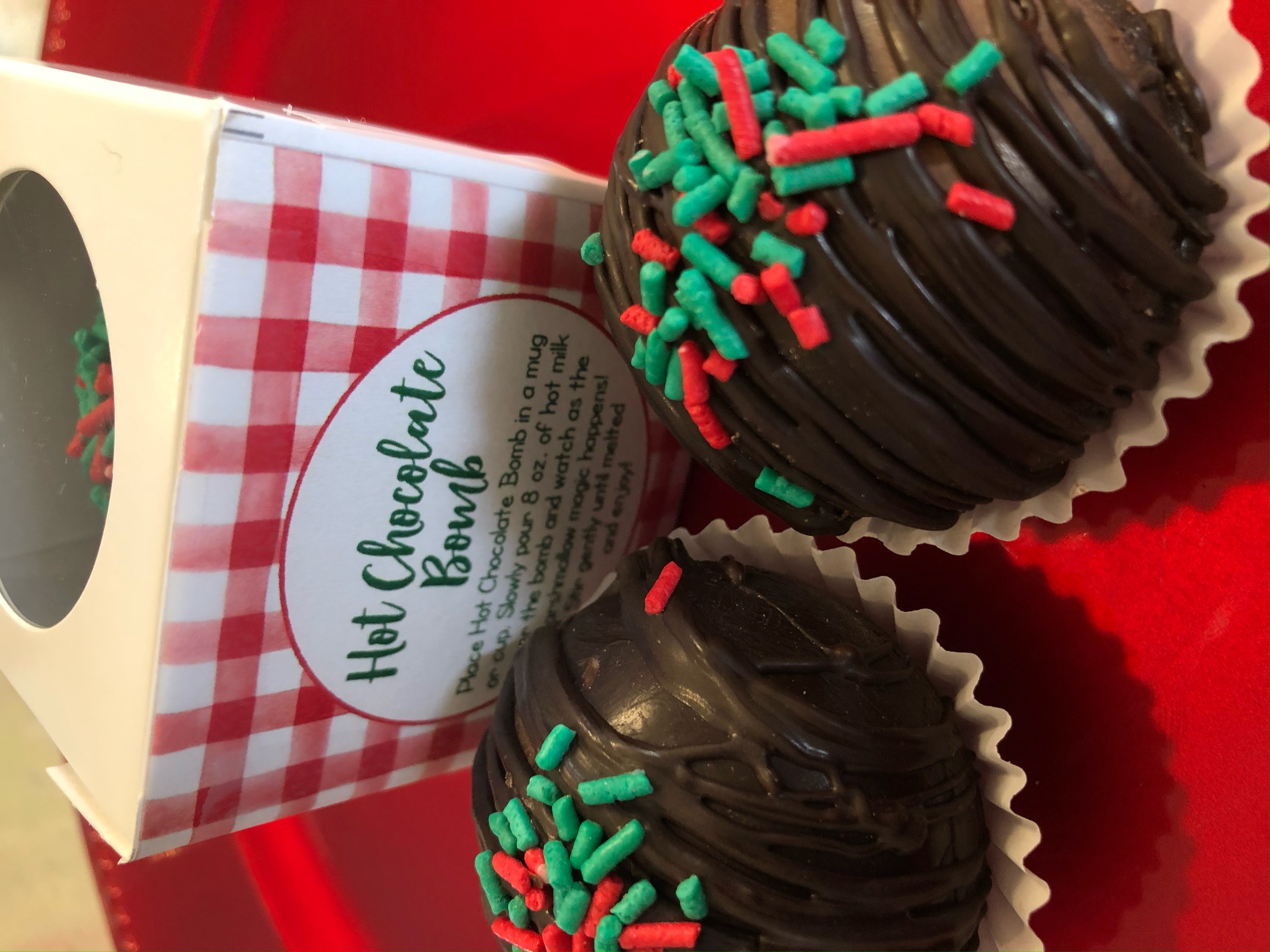 Dark chocolate hot chocolate bombs topped with red and green sprinkles next to their box