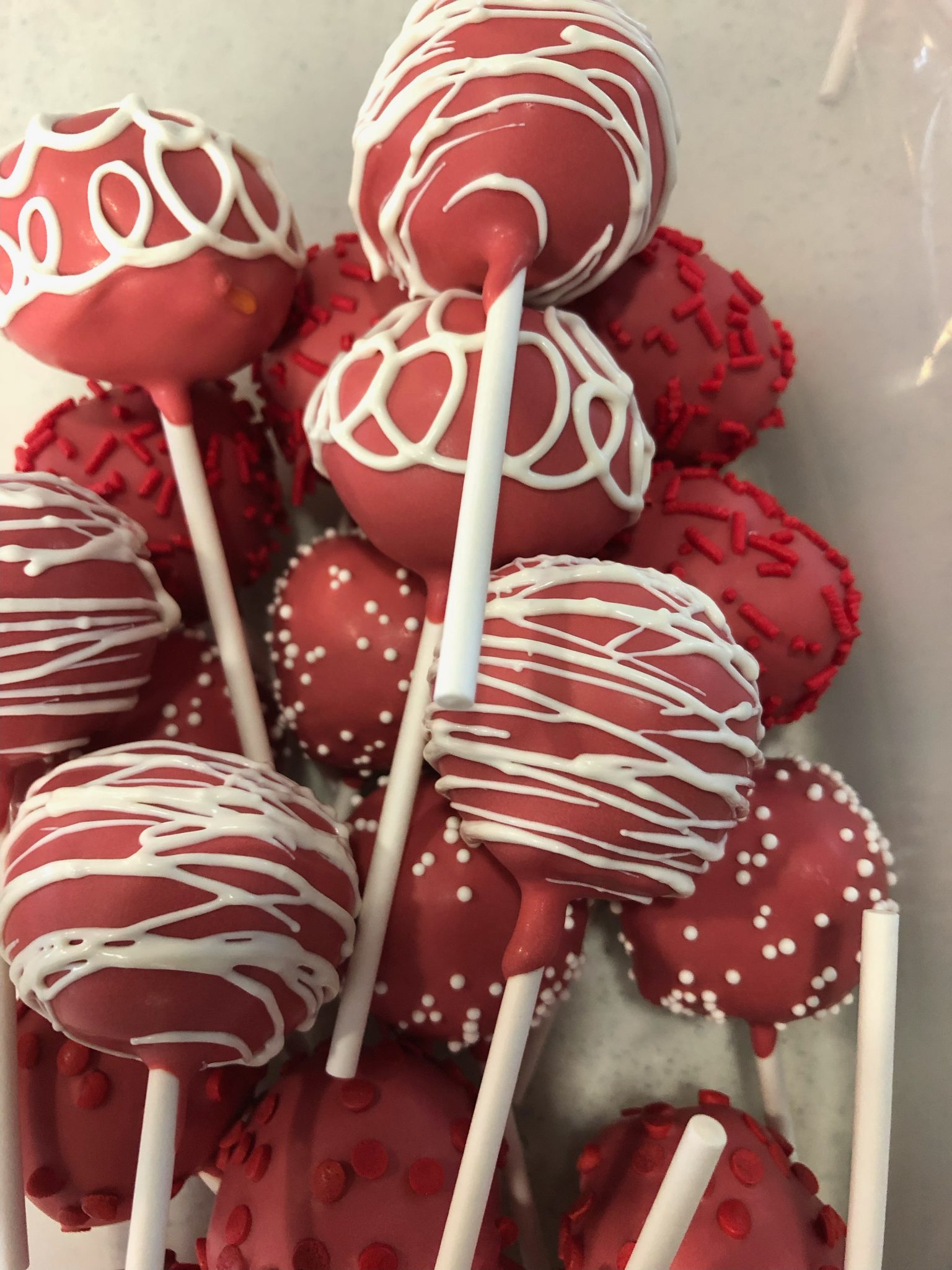 Red cake pops decorated with white drizzle and red sprinkles on white sticks